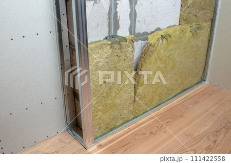 Wall of a room under renovation with mineral rock wool insulation and metal frame prepared for drywall plates. 111422558
