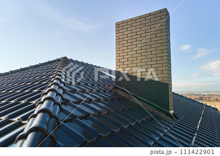 Closeup of brick chimney on house roof top covered with ceramic shingles. Tiled covering of building Closeup of brick chimney on house roof top covered with ceramic shingles. Tiled covering of building 111422901