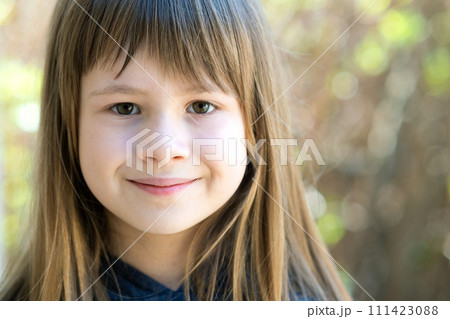 Portrait of pretty child girl with gray eyes and long fair hair smiling outdoors on blurred bright background. Cute female kid on warm summer day outside. Portrait of pretty child girl with gray eyes and long fair hair smiling outdoors on blurred bright background. Cute female kid on warm summer day outside. 111423088