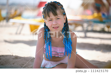 Pretty child girl in bikini swimsuit playing with sand in umbrella shadow during summer tropical vacation 111423170