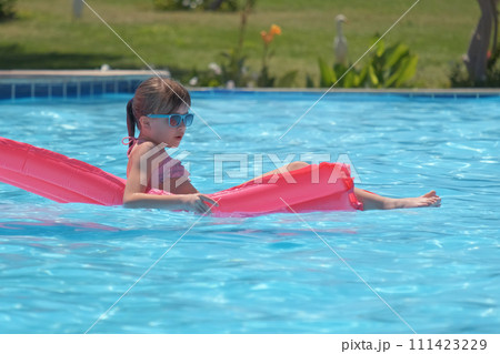 Young child girl relaxing on summer sun swimming on inflatable air mattress in swimming pool during tropical vacations. Summertime activities concept 111423229