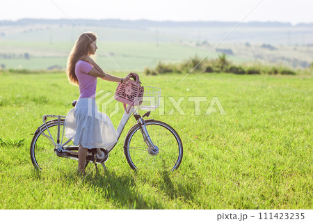 Young woman with a bicycle on green field on a sunny day 111423235