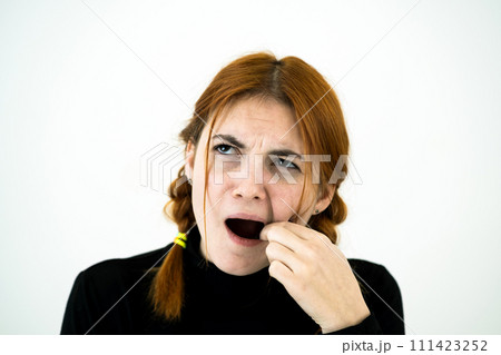 Youn woman with open mouth digging with her fingers for something stuck in teeth after eating. 111423252