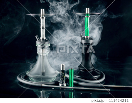 Two modern hookahs with smoke on a black mirror background. 111424211