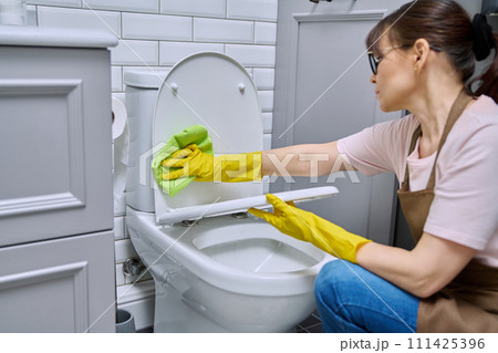 Woman in gloves apron using cleaning detergent clean toilet in bathroom Woman in gloves apron using cleaning detergent clean toilet in bathroom 111425396