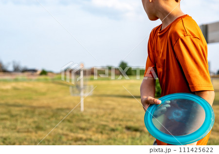 Selective focus fairway grass with a defocused young child holding a putter disc and golf goal in the distance.  Selective focus fairway grass with a defocused young child holding a putter disc and golf goal in the distance.  111425622