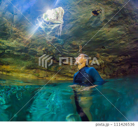 Man immersed in the enchanting beauty of a Mexican cenote, surrounded by crystal-clear waters and captivating natural formations Man immersed in the enchanting beauty of a Mexican cenote, surrounded by crystal-clear waters and captivating natural formations 111426536