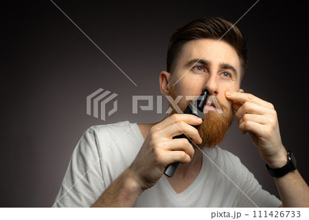 Self-care for men. Handsome young man remove hair from his nose with trimmer Self-care for men. Handsome young man remove hair from his nose with trimmer 111426733