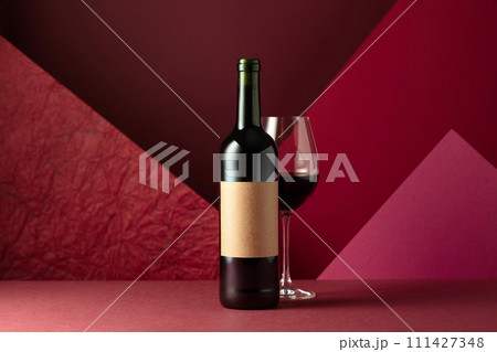 Bottle and glass of red wine on a red background. 111427348