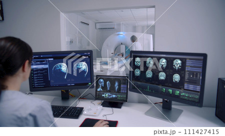 Female radiologist sits in control room and watches at monitors 111427415