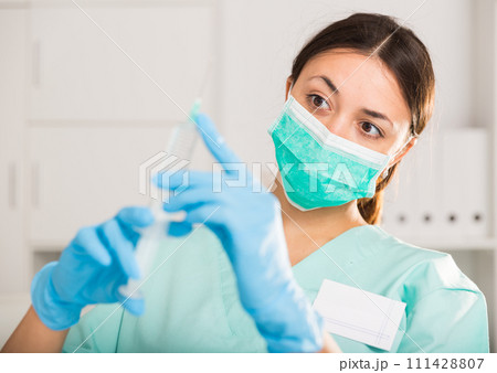 Female nurse in mask holding syringe for injection in hospital Female nurse in mask holding syringe for injection in hospital 111428807