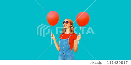 Happy cheerful young woman having fun with balloon wearing red heart shaped sunglasses, jumpsuit Happy cheerful young woman having fun with balloon wearing red heart shaped sunglasses, jumpsuit 111429817