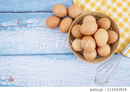 Overhead view of brown chicken eggs in weave basket and a whisk on wooden background. Overhead view of brown chicken eggs in weave basket and a whisk on wooden background. 111432634