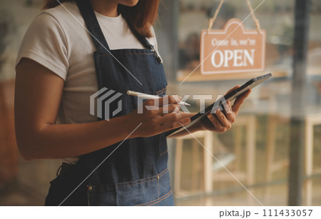 Startup successful small business owner sme beauty girl stand with tablet smartphone in coffee shop restaurant. Portrait of asian tan woman barista cafe owner. SME entrepreneur seller business concept 111433057
