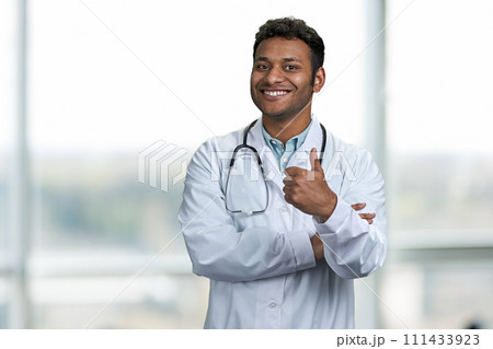Handsome young doctor with stethoscope giving thumb up to camera. Smiling male doctor looking at camera. Handsome young doctor with stethoscope giving thumb up to camera. Smiling male doctor looking at camera. 111433923