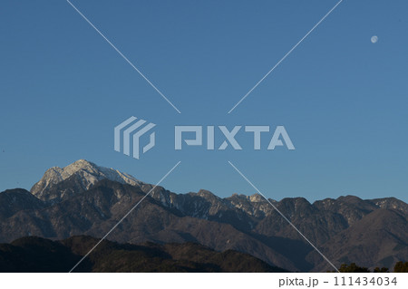 夜明けの空、南アルプス甲斐駒ケ岳の山並みに沈む有明の月 111434034