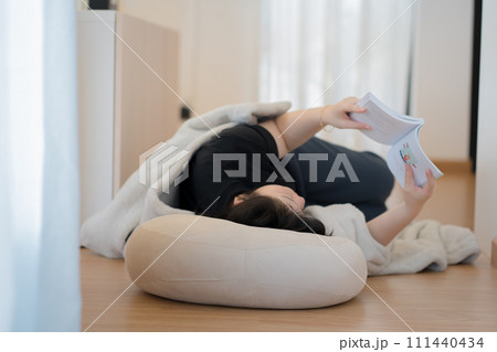 wellness and wellbeing concept with asian woman lie down and read book in livingroom 111440434