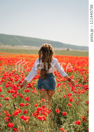 Woman poppies field. Back view of a happy woman with long hair in a poppy field and enjoying the beauty of nature in a warm summer day. 111440786