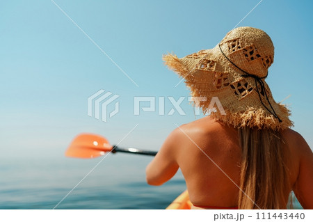 Woman in kayak back view. Happy woman with long hair in a swimsuit and hat floating in kayak on the sea. Summer holiday vacation. Summer holidays vacation at sea. Woman in kayak back view. Happy woman with long hair in a swimsuit and hat floating in kayak on the sea. Summer holiday vacation. Summer holidays vacation at sea. 111443440