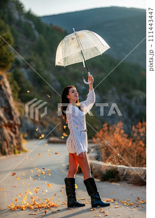 woman umbrella leaves , She holds him over her head, autumn leaves are falling out of him. Beautiful woman in a dress with an umbrella in the autumn park on the road in the mountains. woman umbrella leaves , She holds him over her head, autumn leaves are falling out of him. Beautiful woman in a dress with an umbrella in the autumn park on the road in the mountains. 111443447