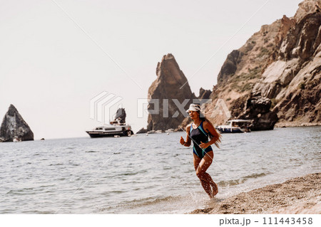 Woman beach vacation photo. A happy tourist in a blue bikini enjoying the scenic view of the sea and volcanic mountains while taking pictures to capture the memories of her travel adventure. Woman beach vacation photo. A happy tourist in a blue bikini enjoying the scenic view of the sea and volcanic mountains while taking pictures to capture the memories of her travel adventure. 111443458
