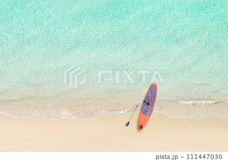 Top view of SUP board for surfing on the shore on tropical Seychelles sand beach. Blue, turquoise transparent water surface of ocean, sea, lagoon. Aerial, drone view 111447030