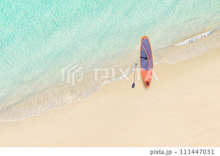 Top view of SUP board for surfing on the shore on tropical Seychelles sand beach. Blue, turquoise transparent water surface of ocean, sea, lagoon. Aerial, drone view 111447031