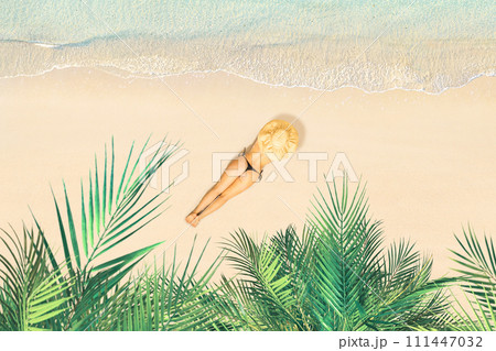 Top view of woman in bikini and straw hat lying and sunbathes on tropical Seychelles sea sand beach with palm tree grove. Aerial, drone view 111447032