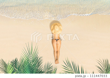 Top view of woman in bikini and straw hat lying and sunbathes on tropical Seychelles sea sand beach with palm tree grove. Aerial, drone view 111447033