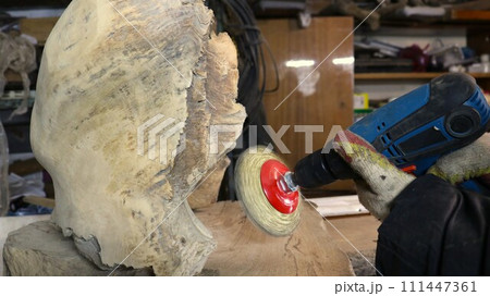 drill with an emery iron brush for wood sanding in the hands of a carpenter in the workshop, a hand tool with a round metal attachment for processing the surface of wooden material 111447361