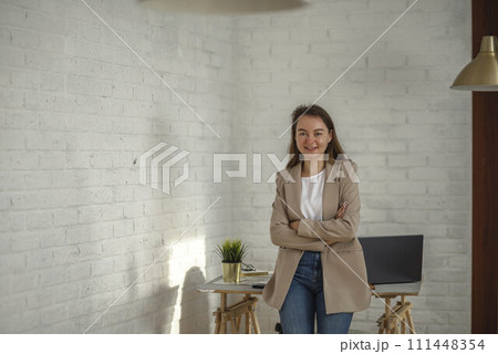 Happy young Businesswoman in Office. Stylish Beautiful Manager Smiling leans on the work table with his arms crossed over her chest Happy young Businesswoman in Office. Stylish Beautiful Manager Smiling leans on the work table with his arms crossed over her chest 111448354