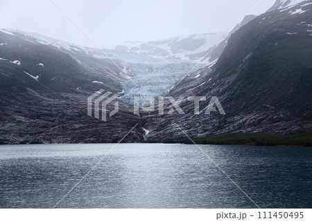 Glistening Svartisen Glacier flows into mirror-like lake, framed by Norway's mountains 111450495