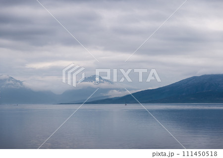 A lone sailboat in vast Norwegian fjord, shrouded peaks loom 111450518