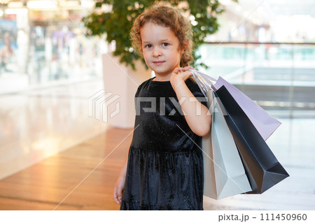cute child girl in black dress on shopping. portrait of a kid with shopping bags. Black Friday concept cute child girl in black dress on shopping. portrait of a kid with shopping bags. Black Friday concept 111450960