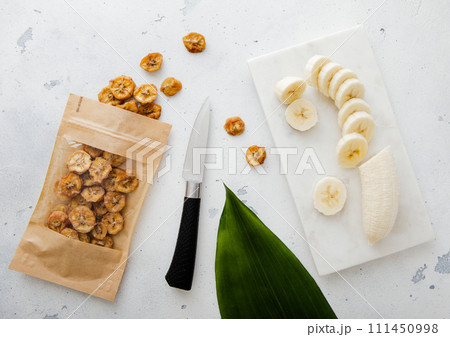 Banana fresh and dried banana slices with leaf and knife on light kitchen background.Top view. 111450998