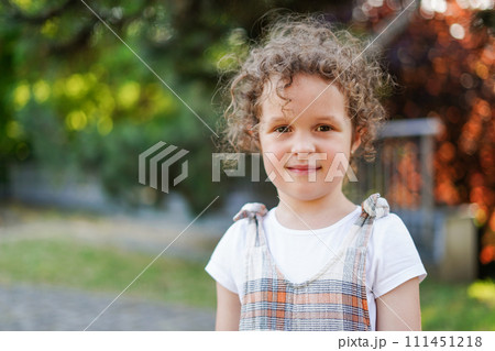 Sweet little girl with curly hair outdoors in the park 111451218