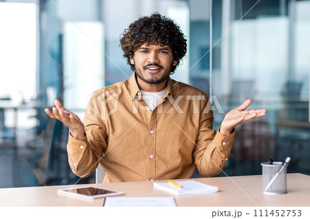 Professional Indian businessman in casual shirt engaging in a discussion at his workplace, bright office setting. 111452753