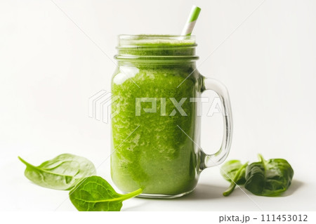 Green detox smoothie in a jar with a straw surrounded by basil leaves on a white background 111453012
