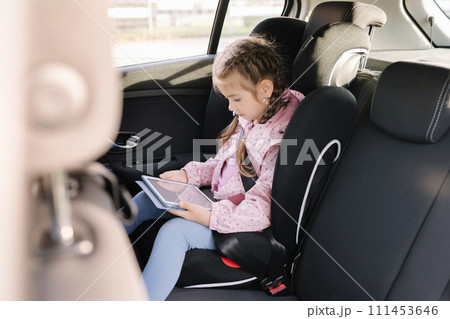 Cute little girl use tablet in car seat on the way to the kindergarten Cute little girl use tablet in car seat on the way to the kindergarten 111453646
