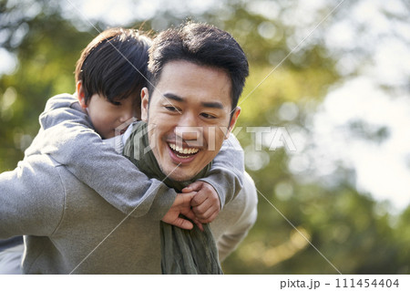 asian loving father carrying son on back walking in park happy and smiling 111454404