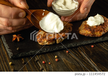Spoon with sour cream in the hand of the cook. Preparing a snack dish with cutlets and sour cream. Food serving concept Spoon with sour cream in the hand of the cook. Preparing a snack dish with cutlets and sour cream. Food serving concept 111454572