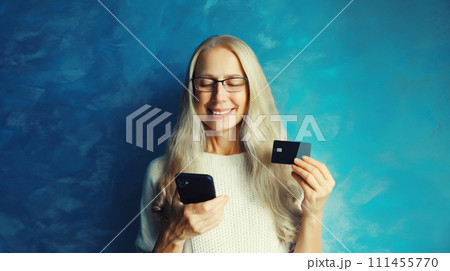 happy middle aged woman shopping online looking at mobile phone holding plastic credit bank card i 111455770