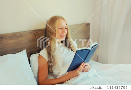 Happy middle aged woman reading book lying on the bed at home Happy middle aged woman reading book lying on the bed at home 111455795