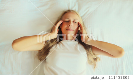 Woman with headache, pain tension in head, suffers from migraine lying in bed at home Woman with headache, pain tension in head, suffers from migraine lying in bed at home 111455805