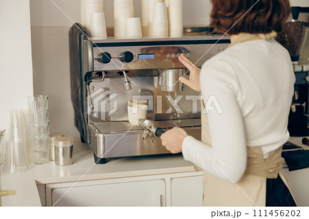 Back view of female barista making coffee in a coffee machine while working in cafe Back view of female barista making coffee in a coffee machine while working in cafe 111456202