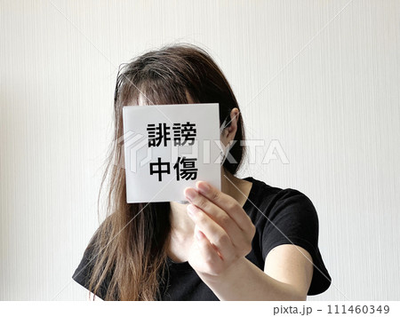 顔の前で誹謗中傷の文字入りの紙を片手で持つ女性 顔の前で誹謗中傷の文字入りの紙を片手で持つ女性 111460349