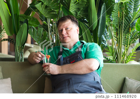 Portrait of an adult man in work clothes drinking a cocktail at lunch while sitting in a cool room Portrait of an adult man in work clothes drinking a cocktail at lunch while sitting in a cool room 111468920