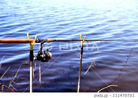Fishing rod on stands against the background of water, close-up, toning Fishing rod on stands against the background of water, close-up, toning 111470781