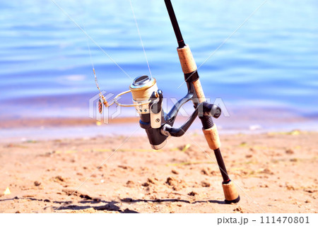 fishing rod with reel on the background of the river, blue water, sun, sand 111470801
