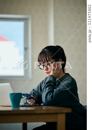 頬杖をついてスマホを操作する若い女性 111473802